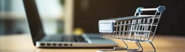 Photo of a miniature shopping cart sitting in front of a laptop computer.